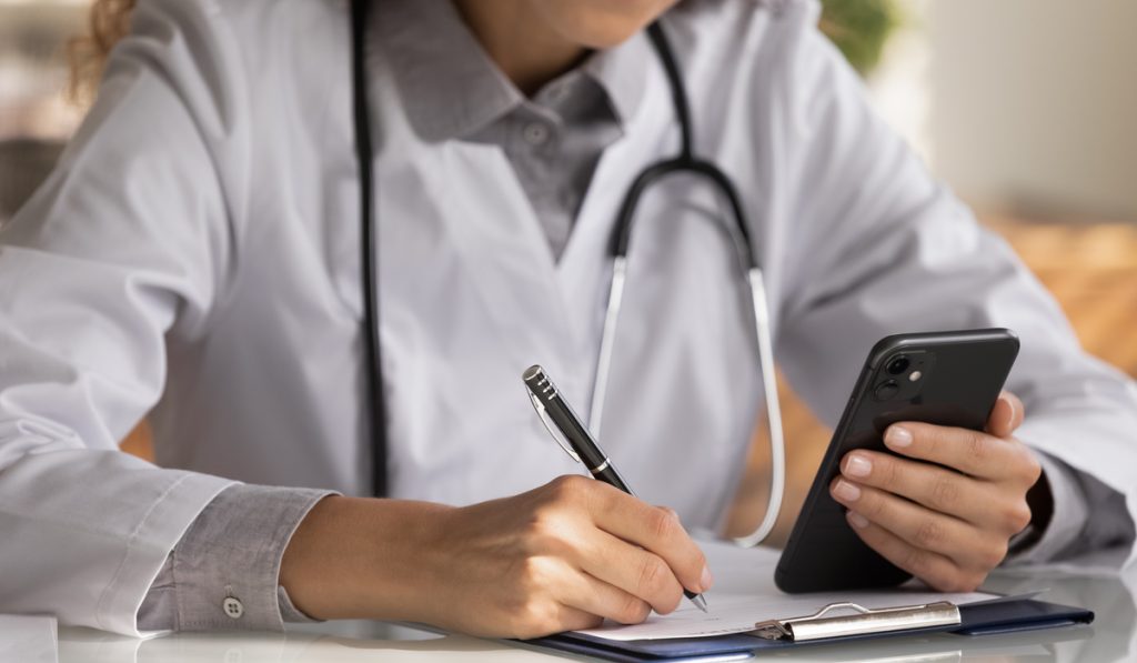 Close up female doctor wearing uniform with stethoscope holding smartphone