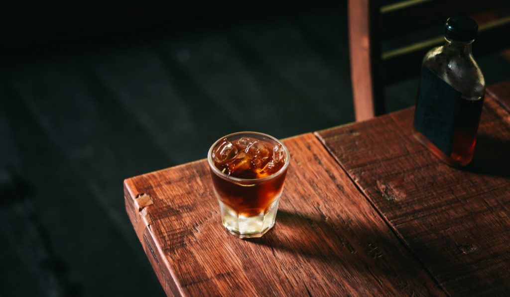 Cold brew coffee with ice cubes and the glass bottle on the wooden table from above