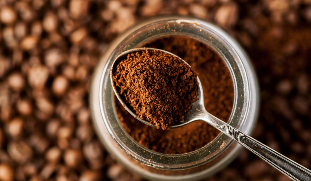 Ground coffee in a metal spoon on a top of glass jar, shallow depth of field.