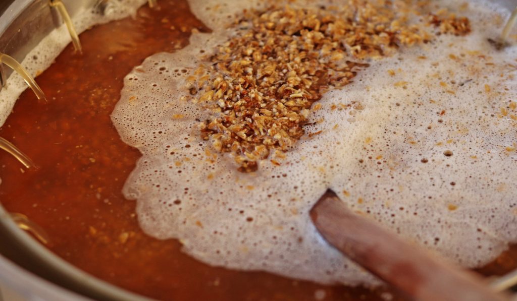Homebrew mashing process showing beer wort, malted barley and wooden spoon