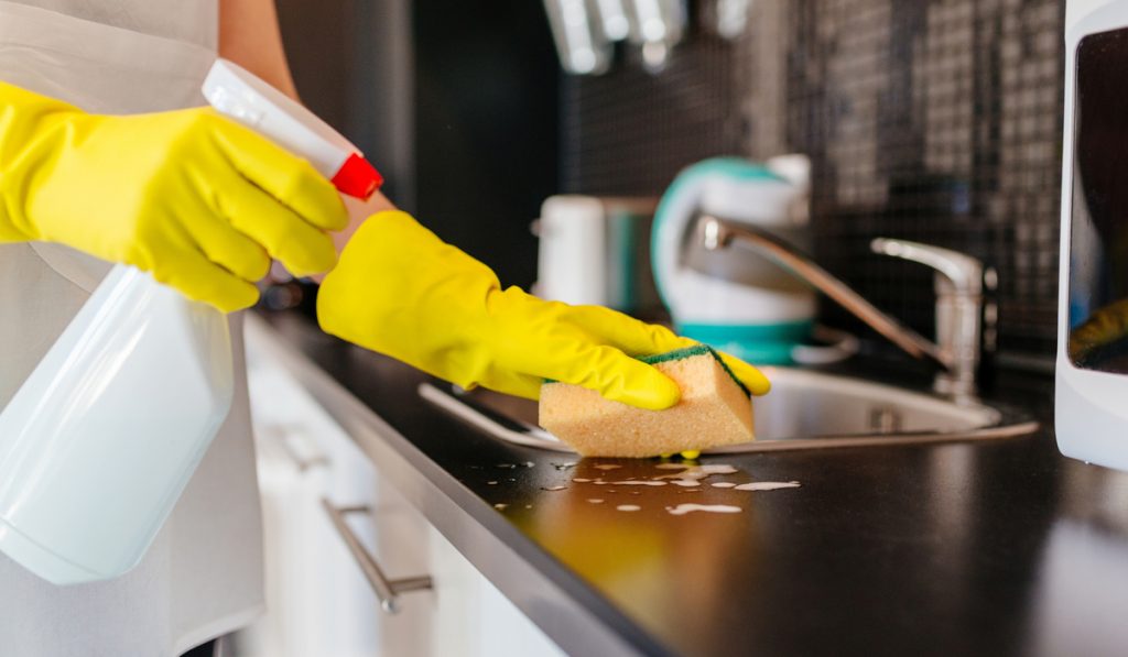 woman wearing gloves cleaning kitchen area sponge spray 